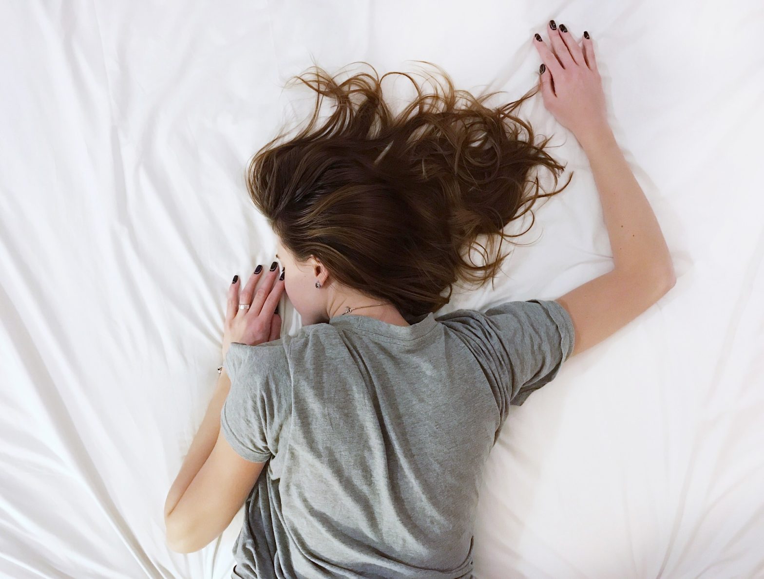Woman in grey tshirt sleeping on white bed sheets