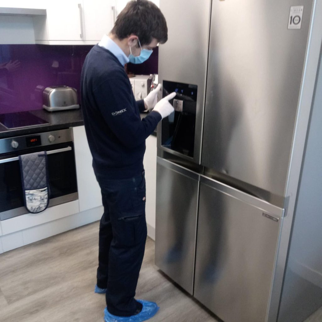 Domex engineer in COVID-19 PPE inspecting fridge freezer