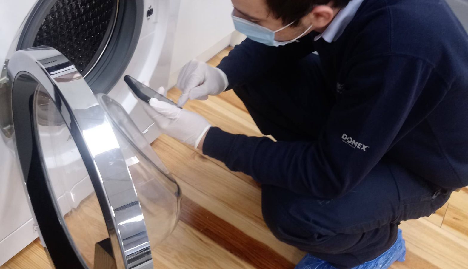 Domex engineer repairing washing machine in COVID-19 safety PPE