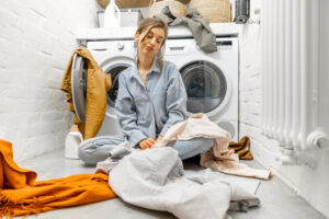 A woman sits on the floor, looking concerned in front of a washing machine, as the tumble dryer fails to heat up