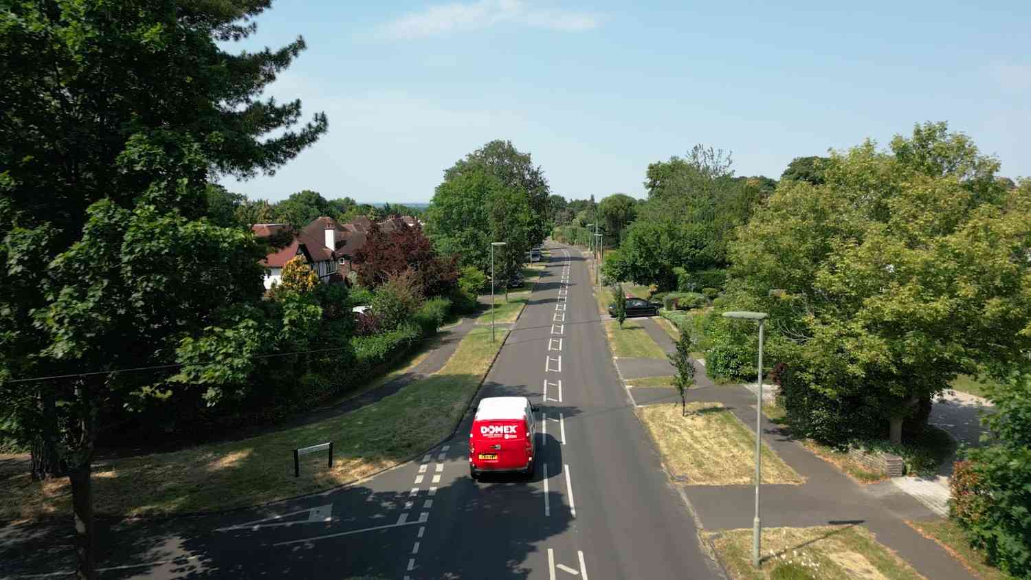 A Domex van drives down a tree-lined suburban road on a clear, sunny day.