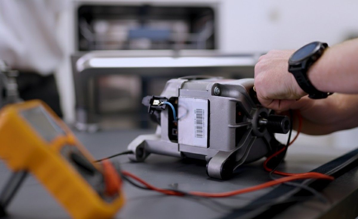 A Domex engineer performing a bench test on a dishwasher circulation pump using a digital multimeter to check electrical resistance