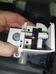 A person holds a small electronic device while testing a washing machine's drain pump functionality