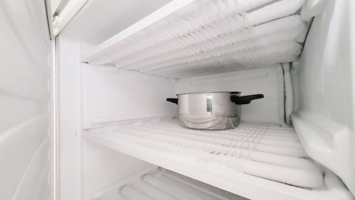 A metal stockpot sits on a frosty shelf inside an open freezer to help melt the ice