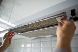Person removing a grease-clogged metal mesh filter from a white kitchen extractor hood