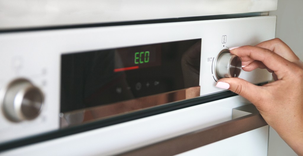 Person setting a white built-in oven to the ECO mode setting