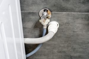 Washing machine cold water inlet hose and drain hose connected to a wall supply tap.