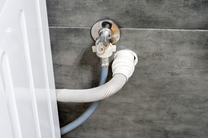 Washing machine cold water inlet hose and drain hose connected to a wall supply tap.